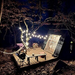 A wooden deck with a table and chairs, string lights, and a small waterfall feature. - Remote Mountain A-Frame with BBQ Perfect for Nature Lovers in West Virginia (Charleston)