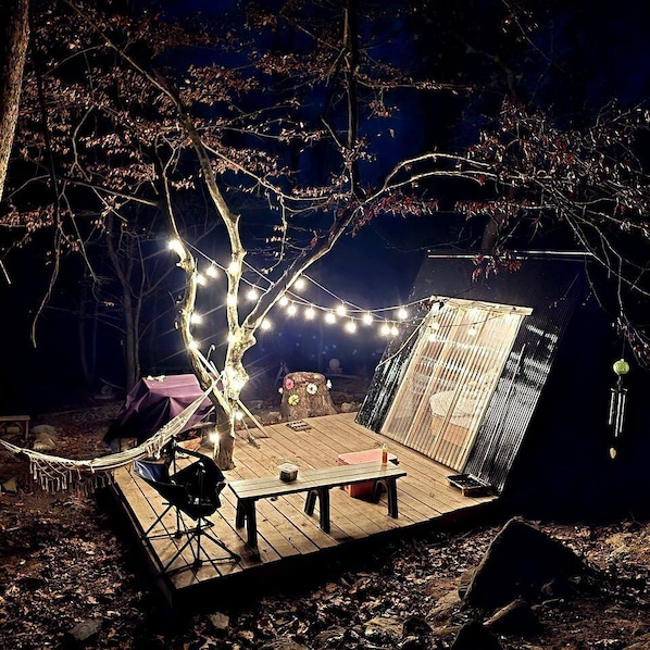 A wooden deck with a table and chairs, string lights, and a small waterfall feature.