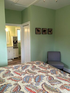 Ein Schlafzimmer mit einem gemusterten Bettbezug, einem grauen Sessel und einer Tür zu einem Badezimmer.