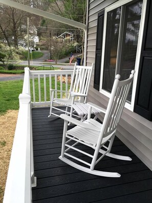 A porch with two rocking chairs and a view of a residential street.