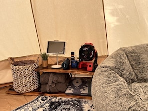 A tent interior with a computer setup, a fan, a storage basket, and a cozy seating area.