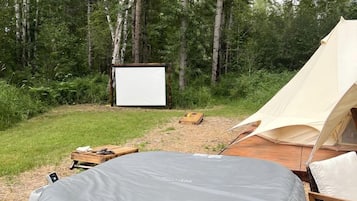 A tent, a covered seating area, and a blank screen in a forested area.