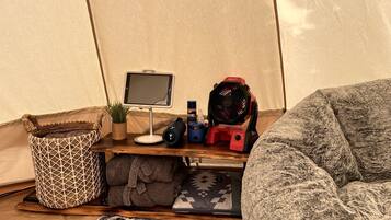 A tent interior with a computer setup, a fan, a storage basket, and a cozy seating area.