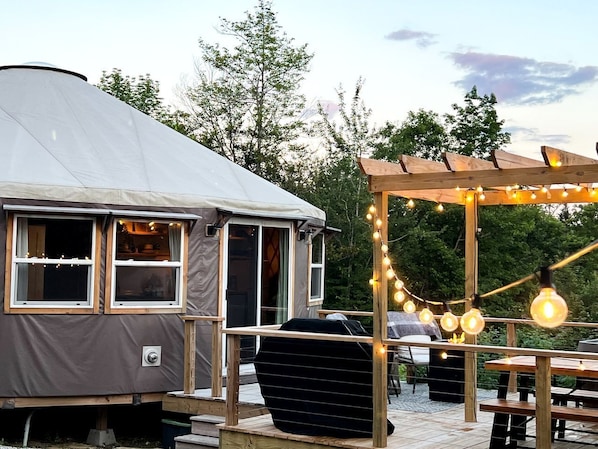A covered outdoor area with a grill, wooden deck, and string lights.