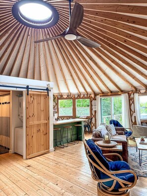 A yurt interior with a central seating area, a kitchen with stools, and a ceiling fan.