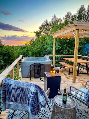 A wooden deck with a hot tub, a fire pit, and outdoor seating.