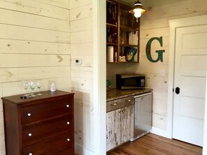 A kitchen with wooden cabinets, a microwave, and a white door with a large green letter 'G'. - Idyllic Cottage on a Working Farm Perfect for Weekend Getaways in Texas (Fayetteville)