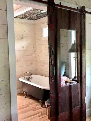 A wooden interior with a bathtub, a mirror, and a wooden floor.