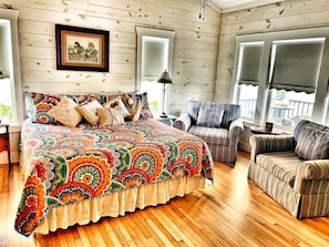 A cozy room with a wooden floor, a large bed with a colorful quilt, a striped armchair, and a framed picture on the wall. - Idyllic Cottage on a Working Farm Perfect for Weekend Getaways in Texas (Fayetteville)