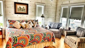 A cozy room with a wooden floor, a large bed with a colorful quilt, a striped armchair, and a framed picture on the wall. - Idyllic Cottage on a Working Farm Perfect for Weekend Getaways in Texas (Fayetteville)