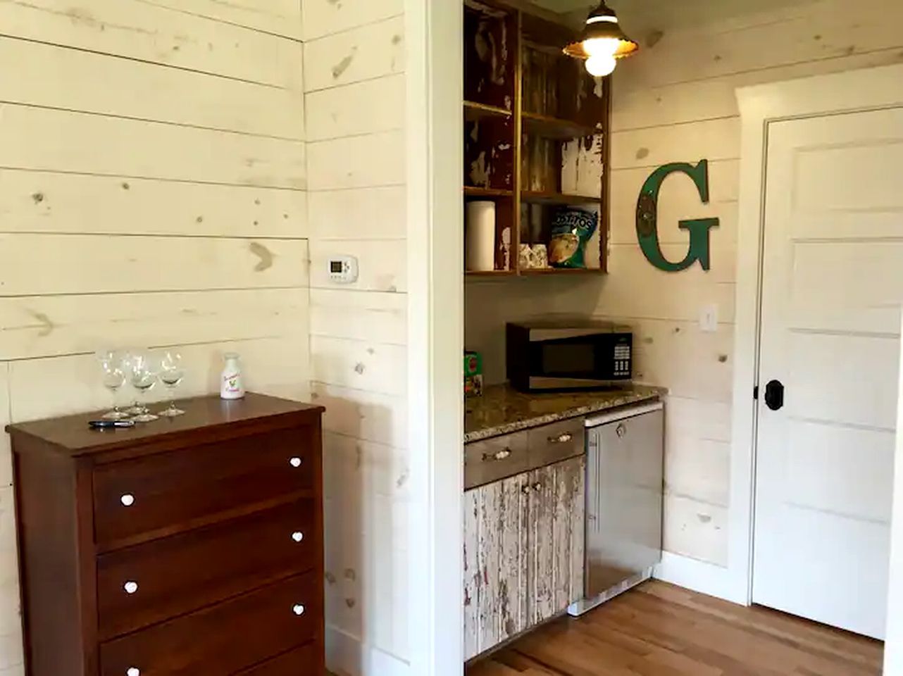 Una cocina con armarios de madera, un microondas y una puerta blanca con una gran letra 'G'.