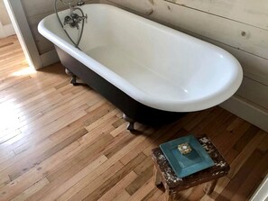 A bathroom with a freestanding bathtub, wooden flooring, and a small blue stool. - Idyllic Cottage on a Working Farm Perfect for Weekend Getaways in Texas (Fayetteville)