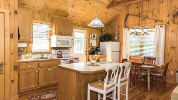 Interior de una cabaña de madera con cocina, comedor y un amplio ventanal.