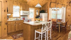A wooden cabin interior with a kitchen, dining area, and a large window.