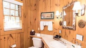 A wooden-paneled bathroom with a toilet, sink, and a framed picture on the wall.
