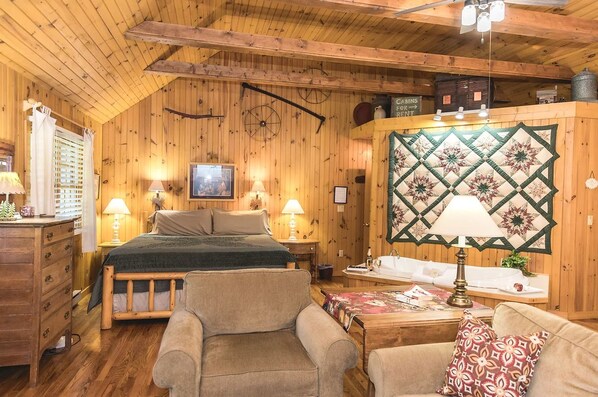 A cozy cabin-style room with a bed, two chairs, a wooden dresser, a quilted wall hanging, and a sign indicating cabins for rent.