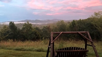 A wooden swing set in a grassy field with a view of distant mountains and trees.