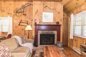 Una habitación acogedora con chimenea, paredes de madera, un sofá, una mesa de centro y una lámpara.
