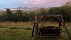 A wooden swing set in a grassy field with a view of distant mountains and trees.