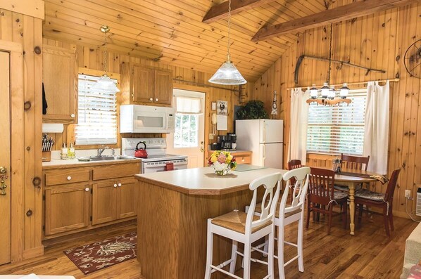 Interior de una cabaña de madera con cocina, comedor y un amplio ventanal.