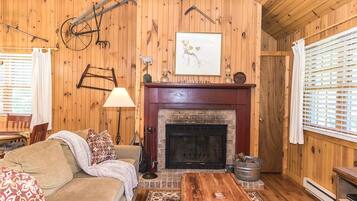 A cozy room with a fireplace, wooden walls, a sofa, a coffee table, and a lamp.