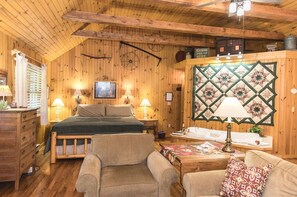 Una habitación acogedora de estilo cabaña con una cama, dos sillones, un aparador de madera, un tapiz acolchado y un cartel que indica cabañas en alquiler.