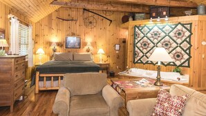 A cozy cabin-style room with a bed, two chairs, a wooden dresser, a quilted wall hanging, and a sign indicating cabins for rent.