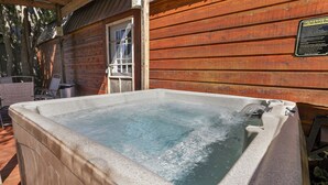 A hot tub outside a wooden cabin with a safety sign.