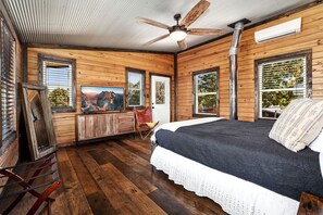 Ein schlicht eingerichtetes Schlafzimmer im Chalet-Stil mit Bett, Deckenventilator, Fernseher und Fenster mit Bergblick.