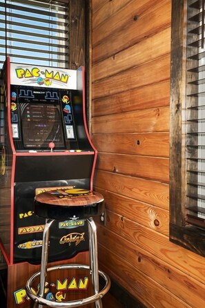 Une borne d’arcade Pac-Man avec un tabouret devant, le tout placé contre un mur en bois.