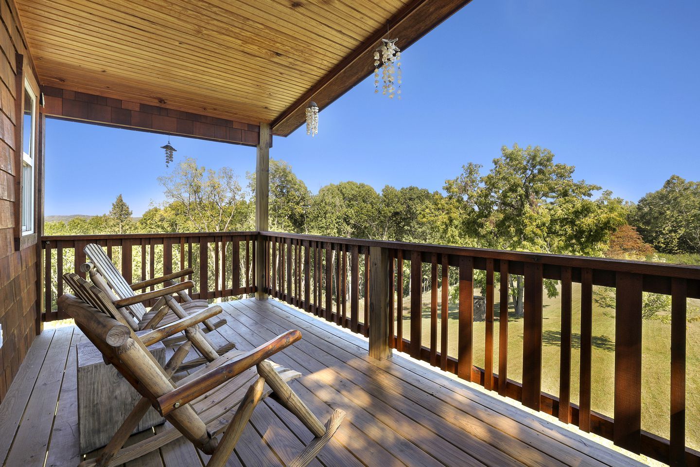 Una terraza de madera con barandilla, zona cubierta y vista a árboles y colinas.