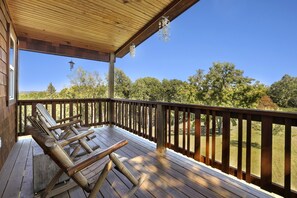 Una terraza de madera con barandilla, zona cubierta y vista a árboles y colinas.