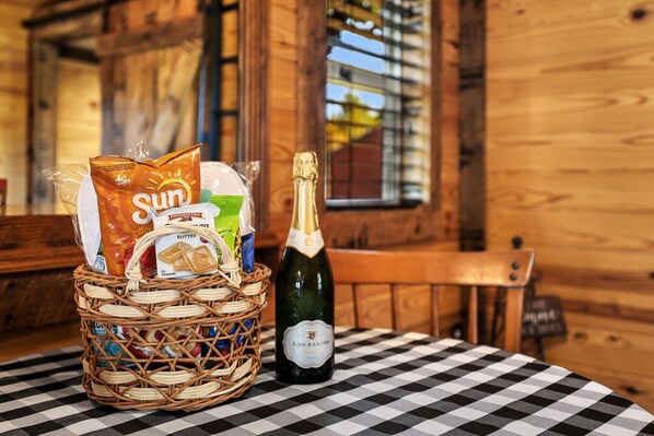 A wicker basket with snacks and a bottle of champagne on a checkered tablecloth in a wooden room.