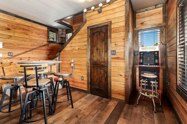 Un intérieur en bois comprenant un bar, un escalier et une borne d’arcade Pac-Man.