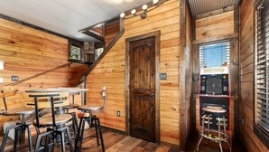 A wooden interior with a bar area, a staircase, and a Pac-Man arcade machine.