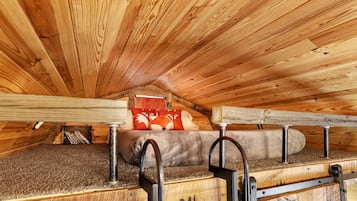 Un dormitorio en el ático con techo de madera, una cama litera y una ventana con cortina.