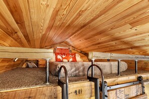 Une chambre mansardée avec un plafond en bois, un lit superposé et une fenêtre avec un rideau.
