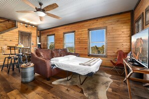 L’intérieur d’une cabane en rondins, avec un canapé, une table à manger, des chaises, un téléviseur et un ventilateur de plafond.