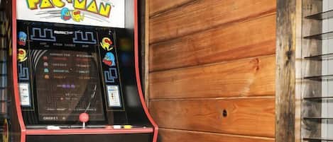 Una máquina arcade de Pac-Man con un taburete al frente, frente a una pared de madera.
