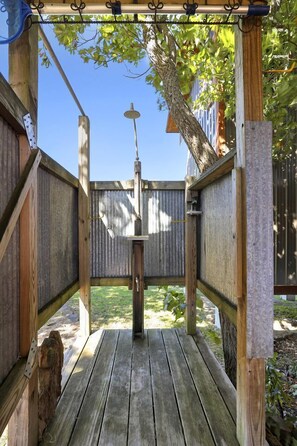 Une terrasse en bois avec une rambarde en métal, un luminaire suspendu et une clôture en bois en arrière-plan.
