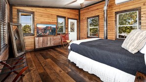 A wooden cabin-style bedroom with a bed, a ceiling fan, a TV, and a window with a mountain view.