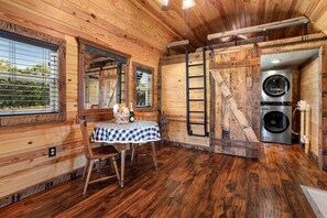 Ein Holzblockbau-Innenraum mit Esstisch, Stühlen, einer Leiter und einer Waschmaschine.