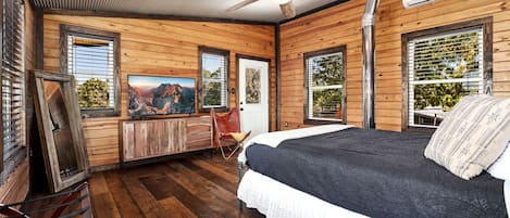 Ein schlicht eingerichtetes Schlafzimmer im Chalet-Stil mit Bett, Deckenventilator, Fernseher und Fenster mit Bergblick.