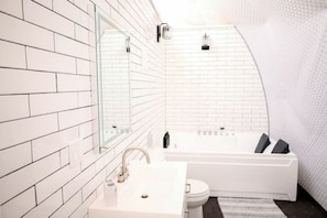 A modern bathroom with white tiled walls, a large mirror, a bathtub, and a toilet.