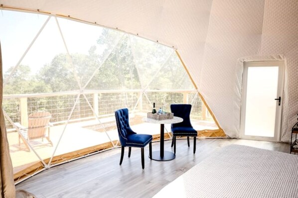 A tented room with a table and chairs, a door, and a view of the outdoors.
