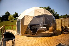 Een koepeltent met een transparante zijkant, een terras en buitengemeubilair.