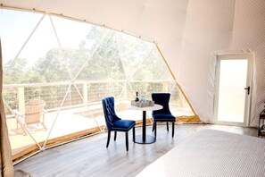 Een tent met een tafel, stoelen, een deur en uitzicht op de omgeving.