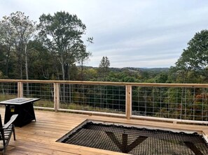 Een houten terras met een tafel en stoelen, omgeven door een hek van gaas, met uitzicht op een bebost landschap.