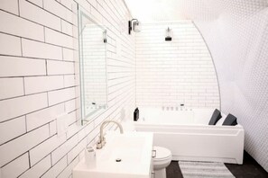 Une salle de bain moderne avec des murs recouverts de carreaux blancs, un grand miroir, une baignoire et des toilettes.