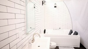 Un baño moderno con paredes de azulejos blancos, un espejo grande, una bañera y un inodoro.